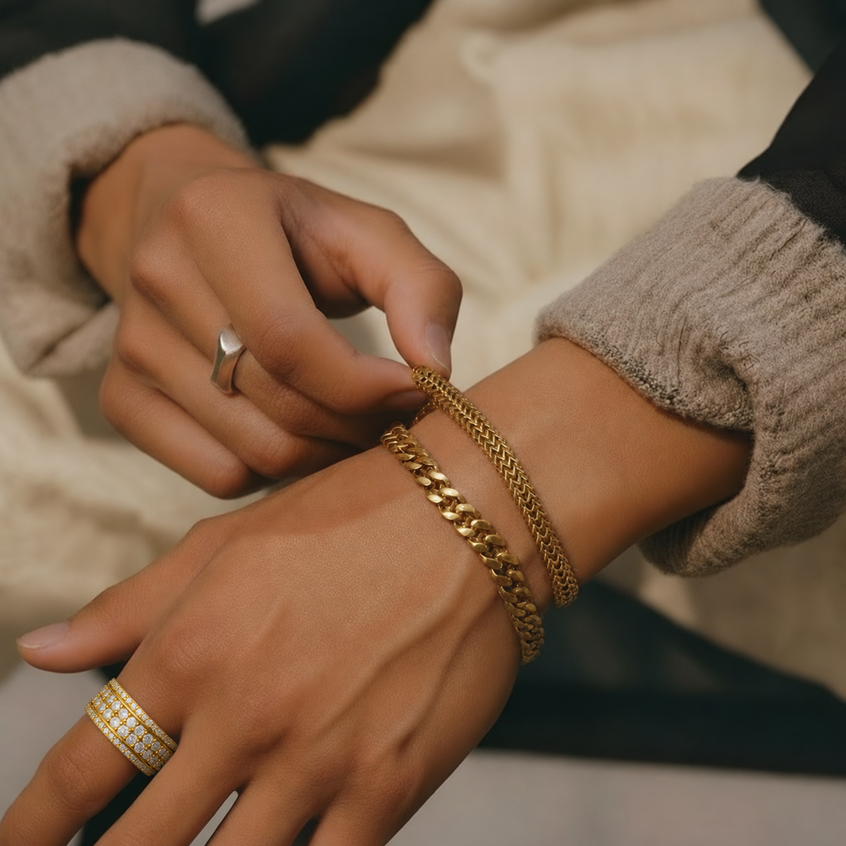 A close-up of a person's hands and wrists wearing multiple yellow-gold bracelets, including a chunky curb chain bracelet and a thinner braided bracelet, with Cassian ring in yellow-gold
variant: yellow-gold