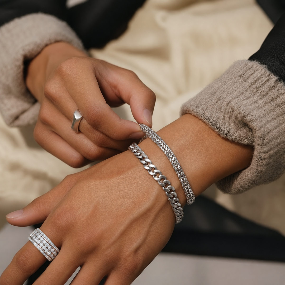 A close-up of a person's hands and wrists wearing multiple silver-toned bracelets, including a chunky curb chain bracelet and a thinner braided bracelet, with Cassian ring in silver
variant: silver