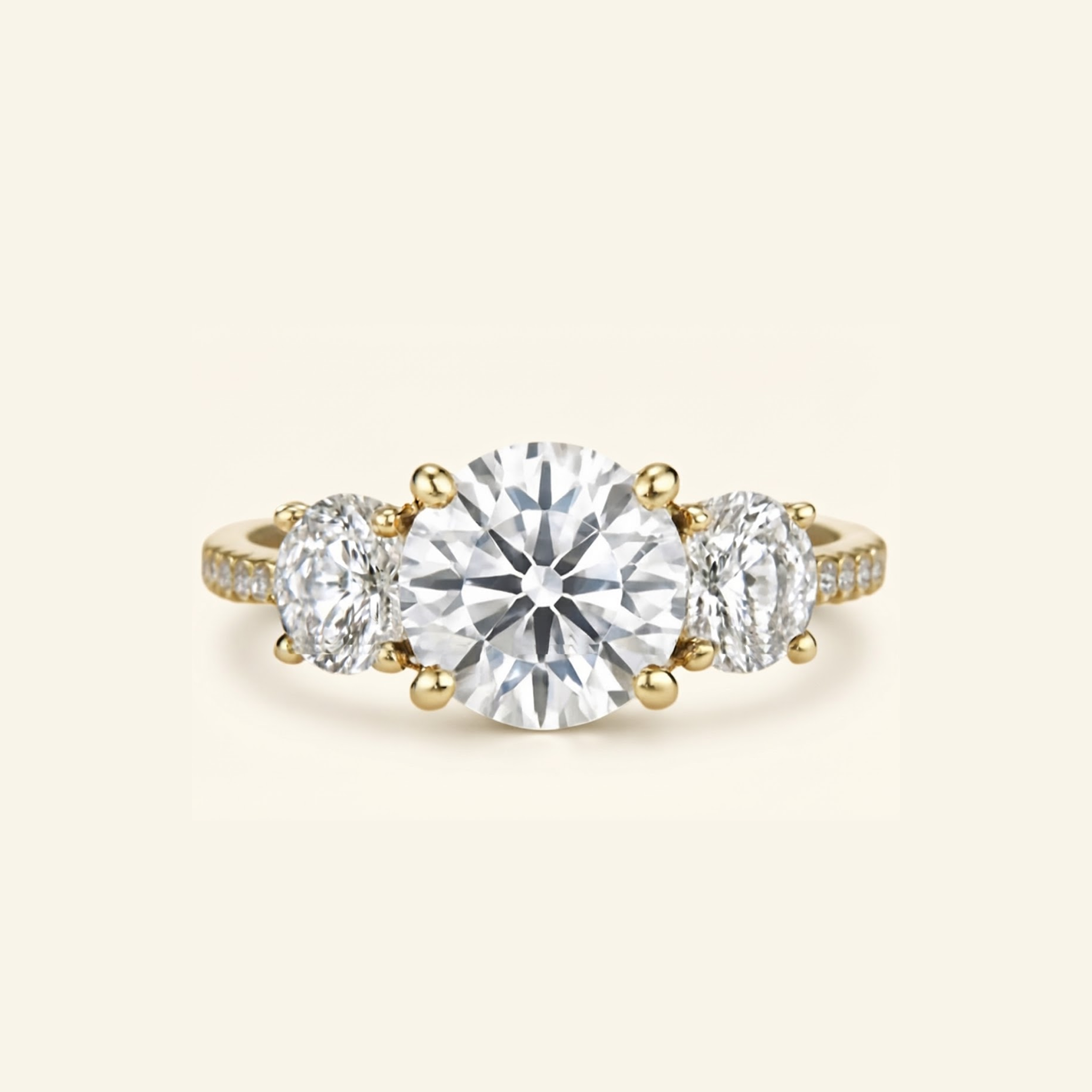 Celia in gold, a three-stone ring featuring a large round-cut center diamond flanked by two oval side diamonds, with small pavé accents on the band, set against a solid cream background.

variant: yellow-gold