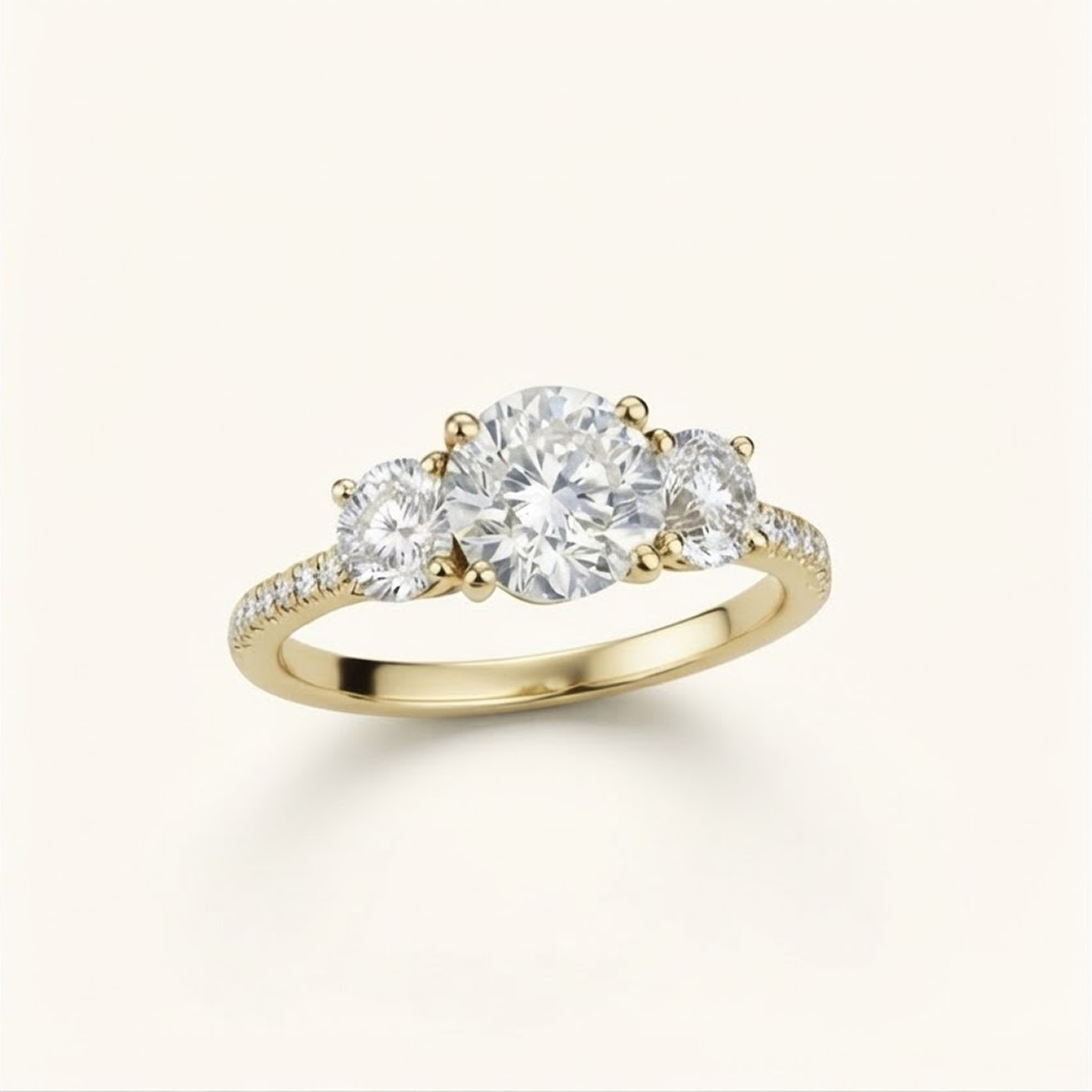 Celia Ring in white gold at an angle, a three-stone diamond engagement ring with a large round center diamond and two smaller round side diamonds, set on a slim pavé-set band, shown on a light cream background.

variant: yellow-gold