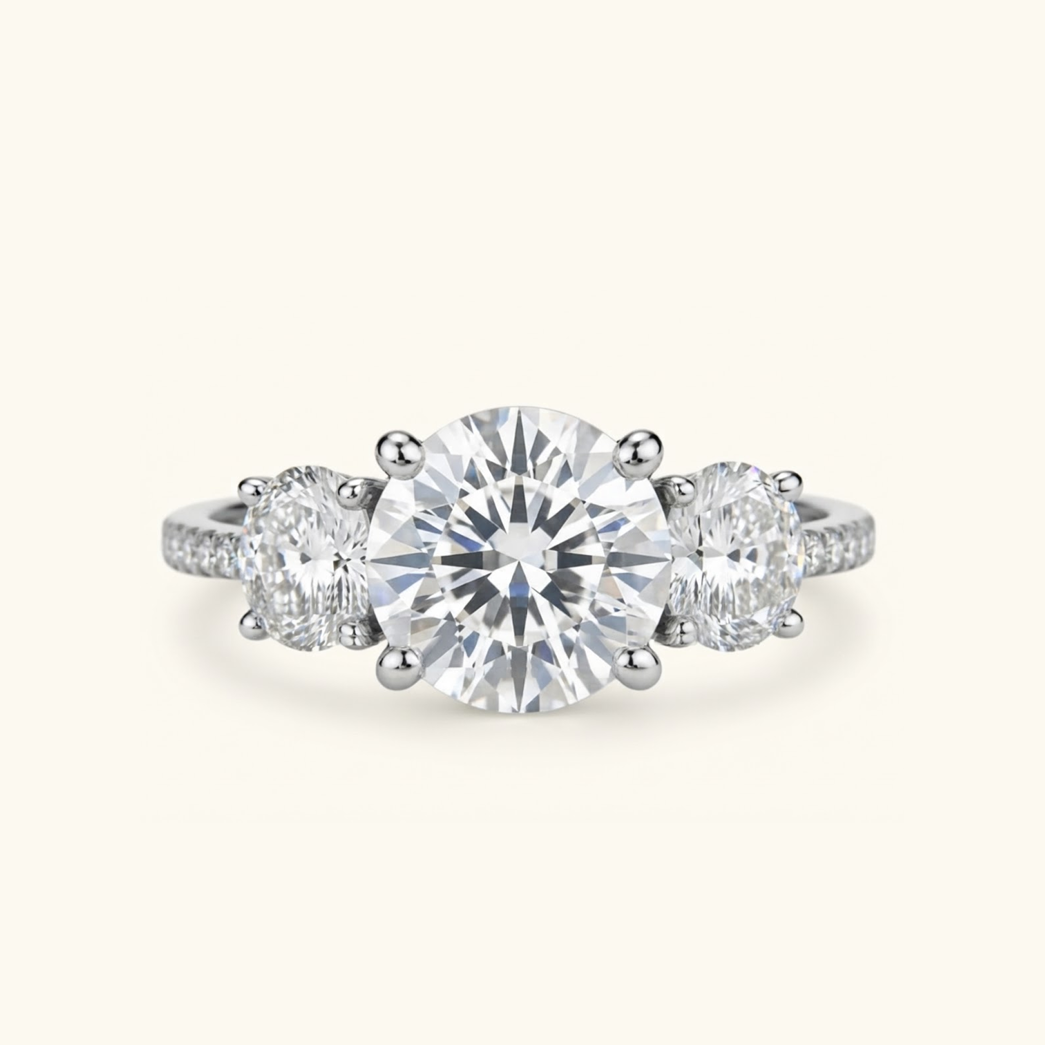 Celia Ring in silver or platinum with a round brilliant center diamond, two oval side stones, and a pavé band, on a cream background.

variant: silver