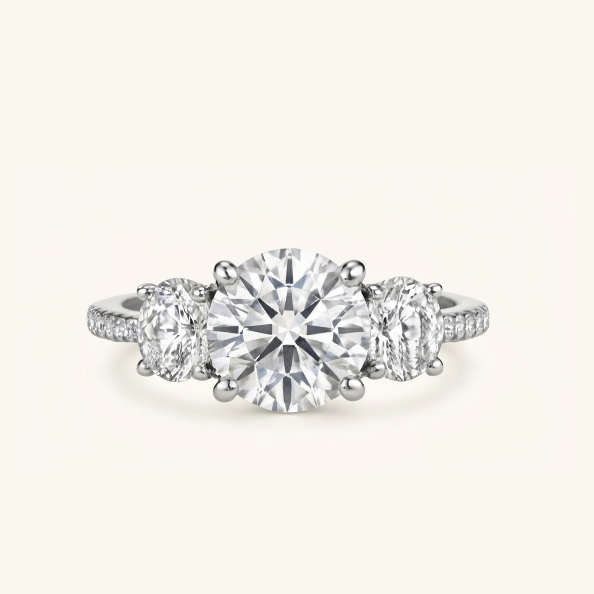 Celia Ring in white gold with a round brilliant center diamond, two oval side stones, and a pavé band, on a cream background.

variant: white gold