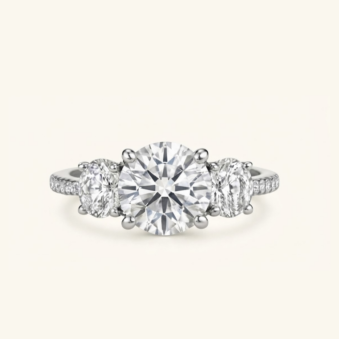Celia Ring in white gold with a round brilliant center diamond, two oval side stones, and a pavé band, on a cream background.

variant: white gold