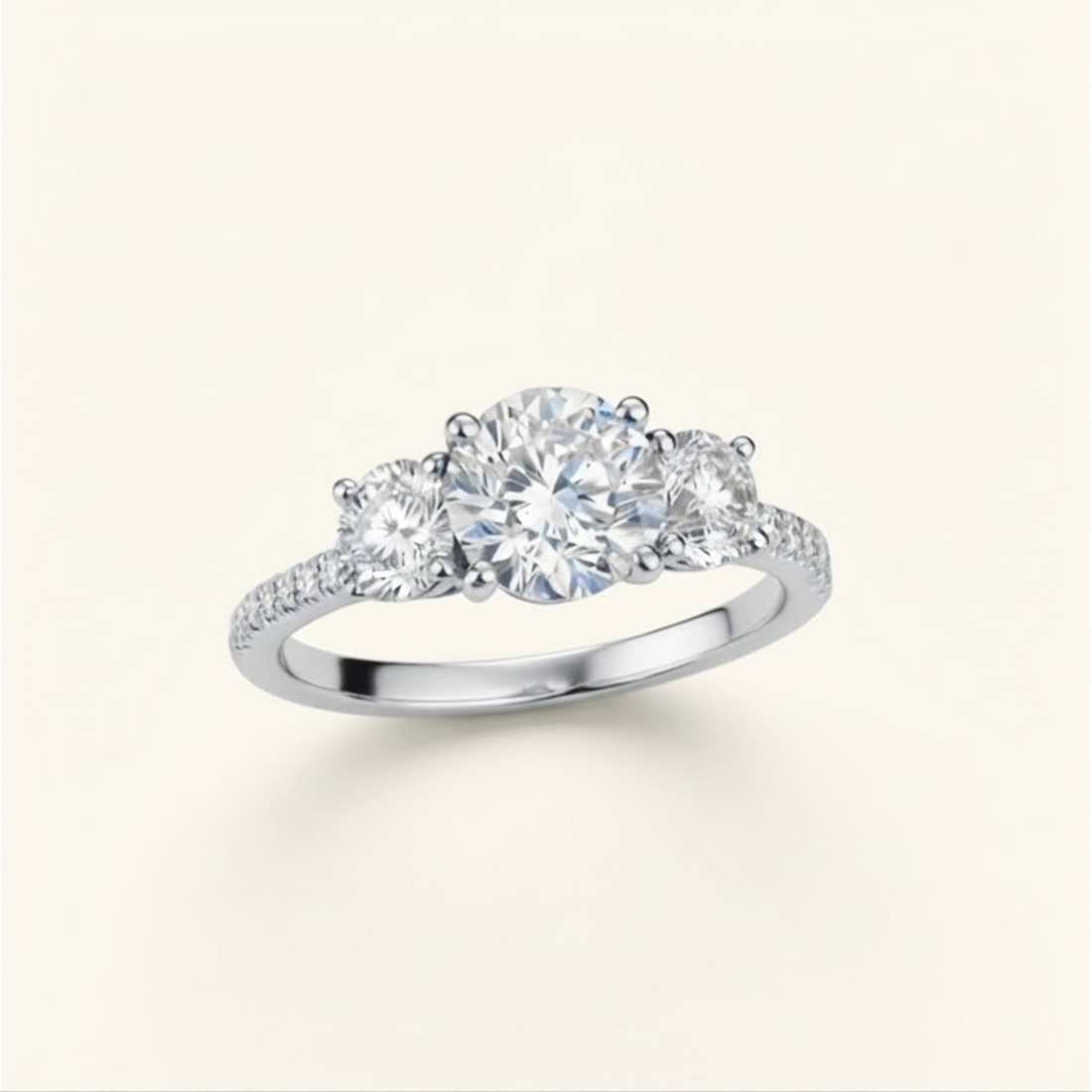 Celia Ring in white gold at an angle, showing the round center diamond, two side stones, and pavé band, on a cream background.

variant: white-gold