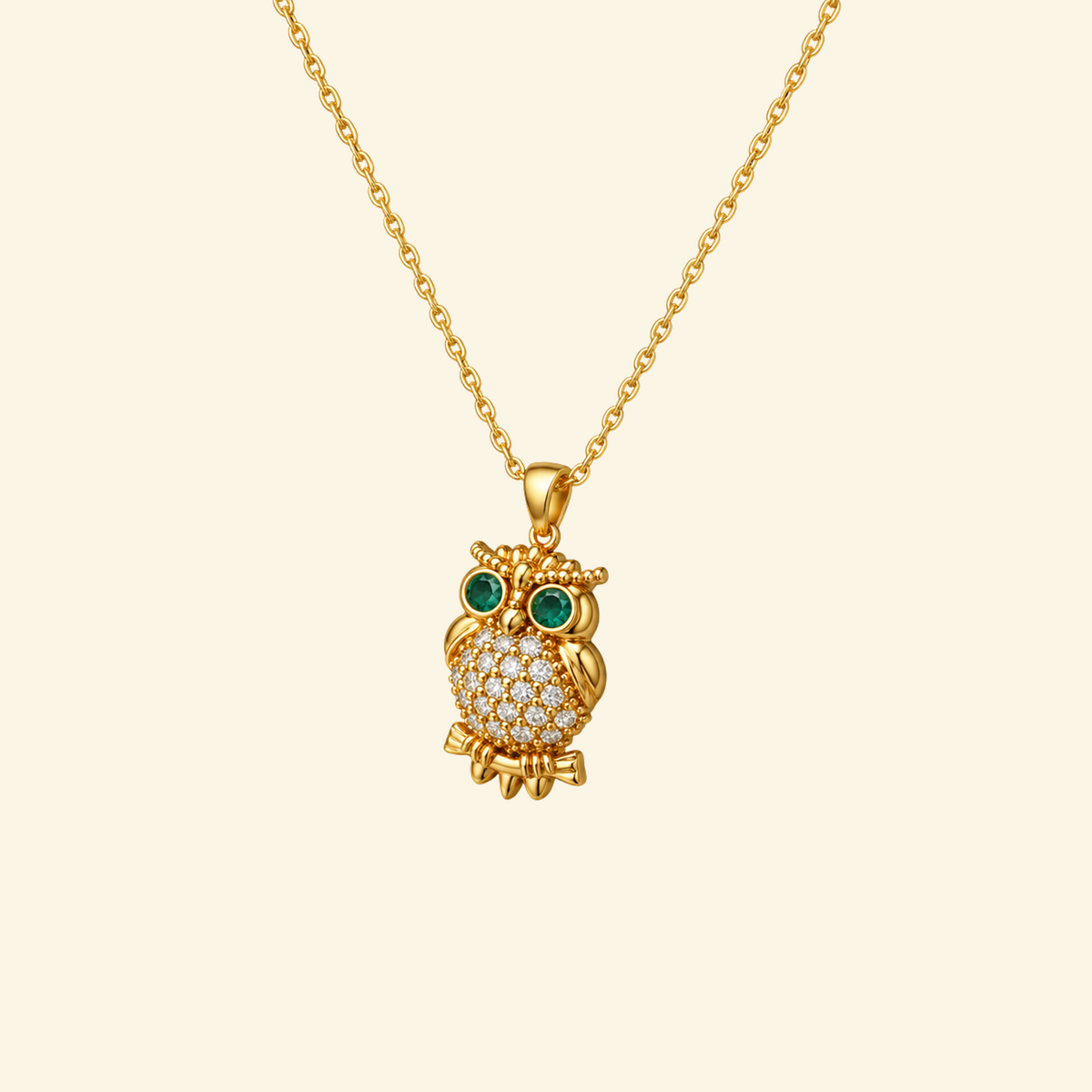Elowen Necklace in yellow gold, a pavé owl pendant with green stone eyes on a fine cable chain, on a cream background.
variant: yellow-gold