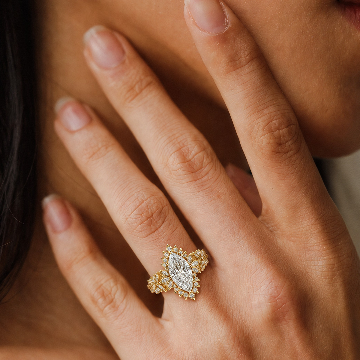 Flora Ring in yellow gold, a marquise diamond with a starburst halo and leaf-inspired band, worn on a hand resting against the face.
variant: yellow-gold