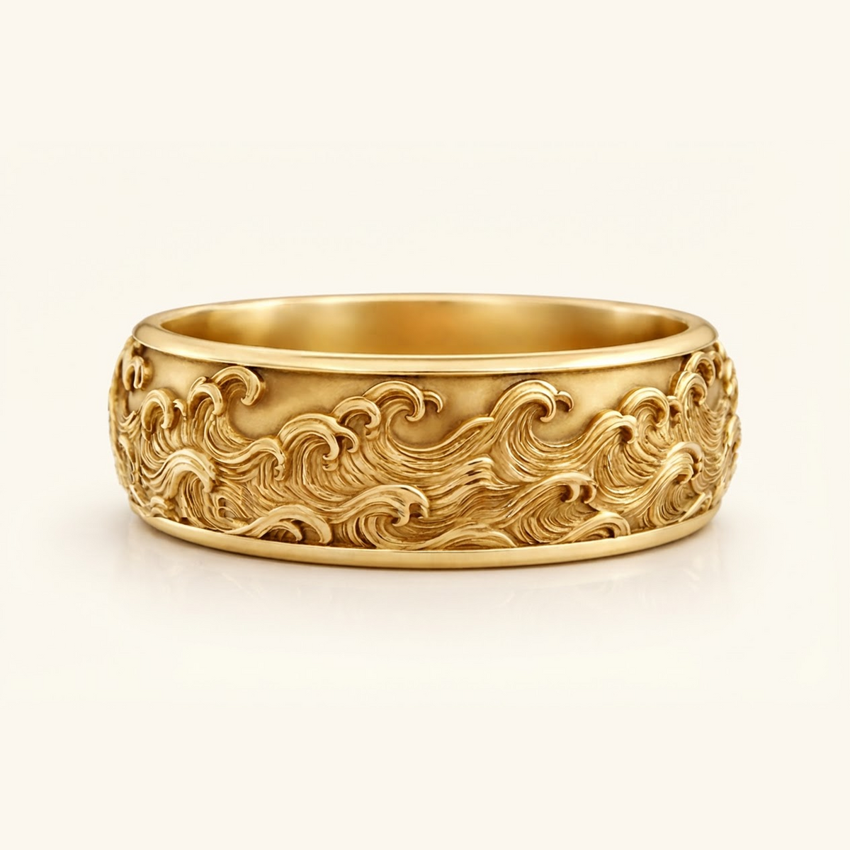 Kai Ring in yellow gold, a wide band with a carved ocean wave relief wrapping the surface, on a cream background.
variant: yellow-gold
