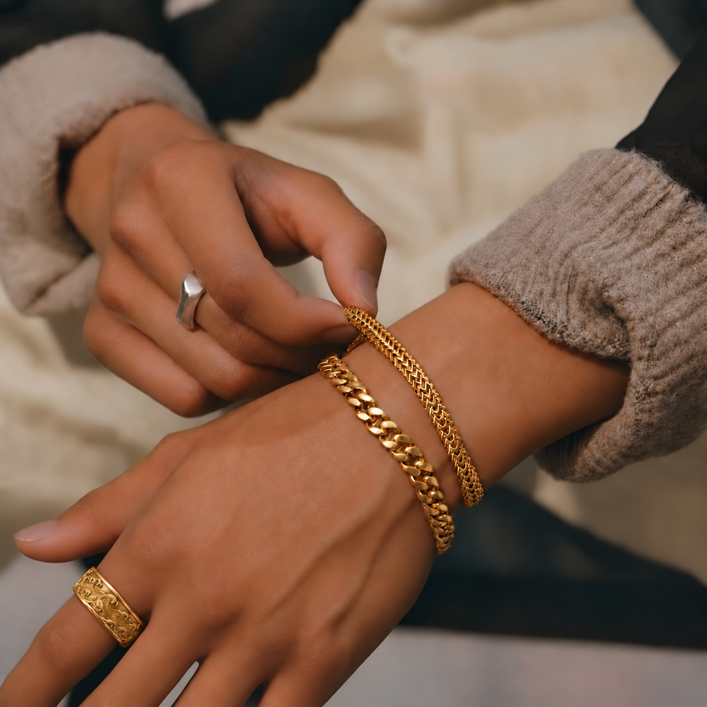 Kai Ring in yellow gold, a wide wave-carved band, worn with two silver chain bracelets as the other hand adjusts them.
variant: yellow-gold