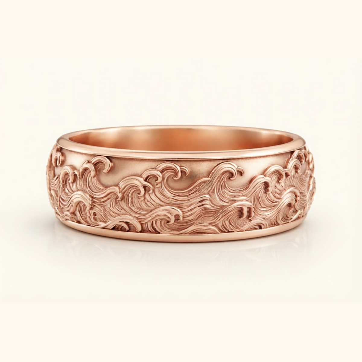 Kai Ring in rose gold, a wide band with a carved ocean wave relief wrapping the surface, on a cream background.
variant: rose-gold