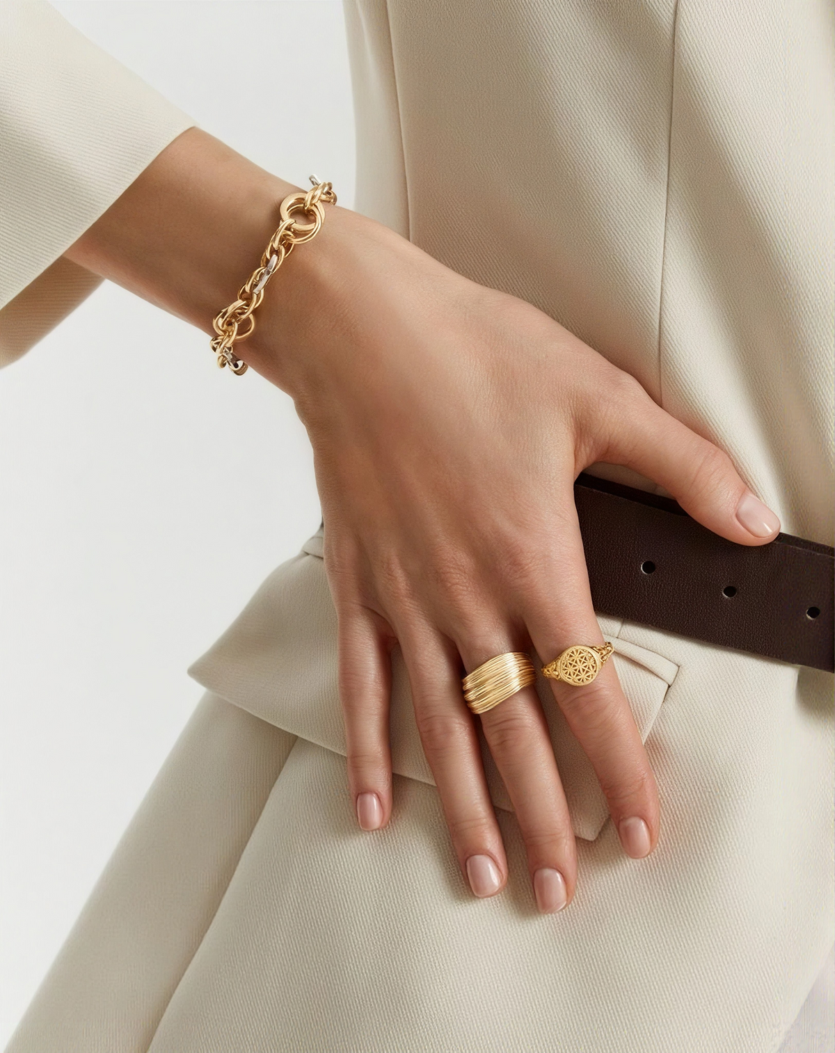 Hand wearing gold jewelry with a neutral background