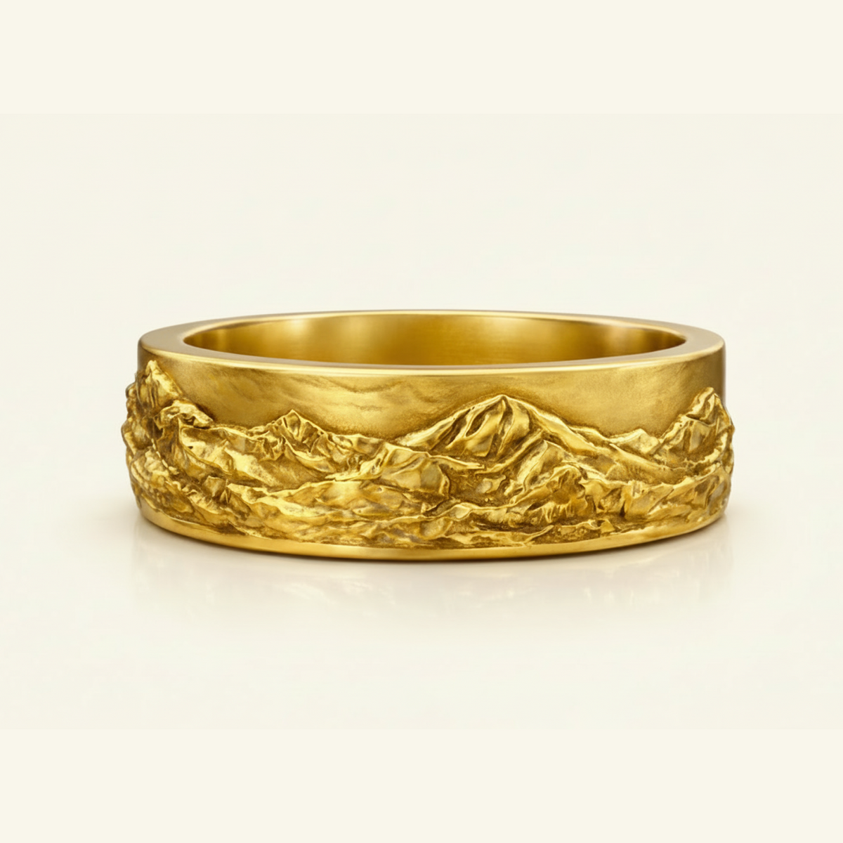 Magnus Ring in yellow gold, a wide band with a sculpted mountain landscape relief wrapping the surface, on a cream background.
variant: yellow-gold