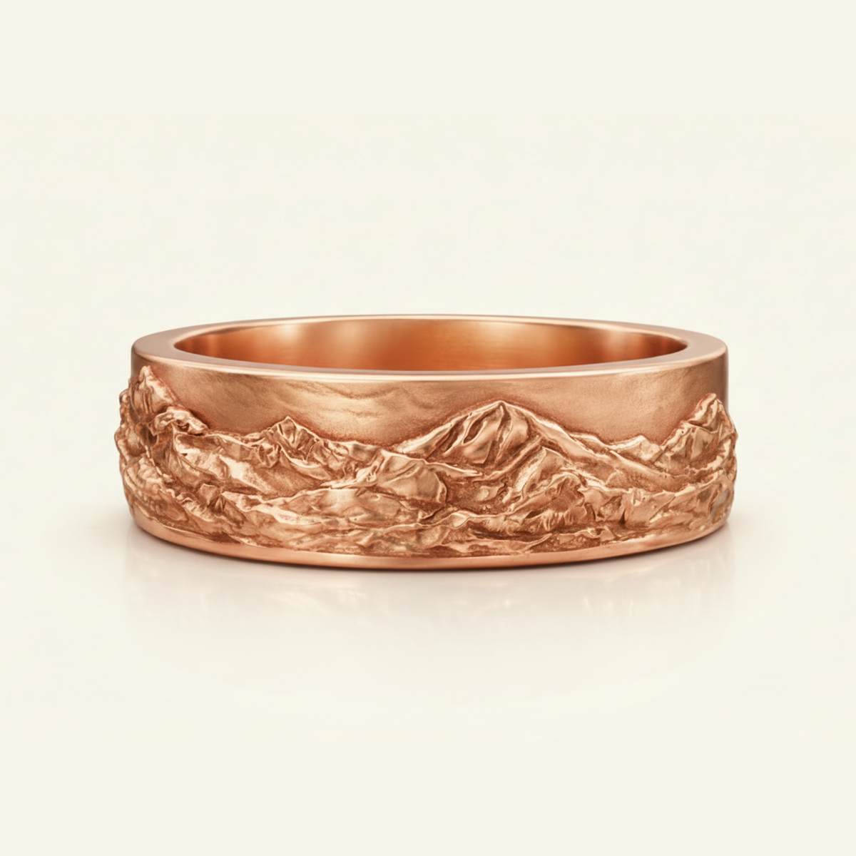 Magnus Ring in rose gold, a wide band with a sculpted mountain landscape relief wrapping the surface, on a cream background.
variant: rose-gold