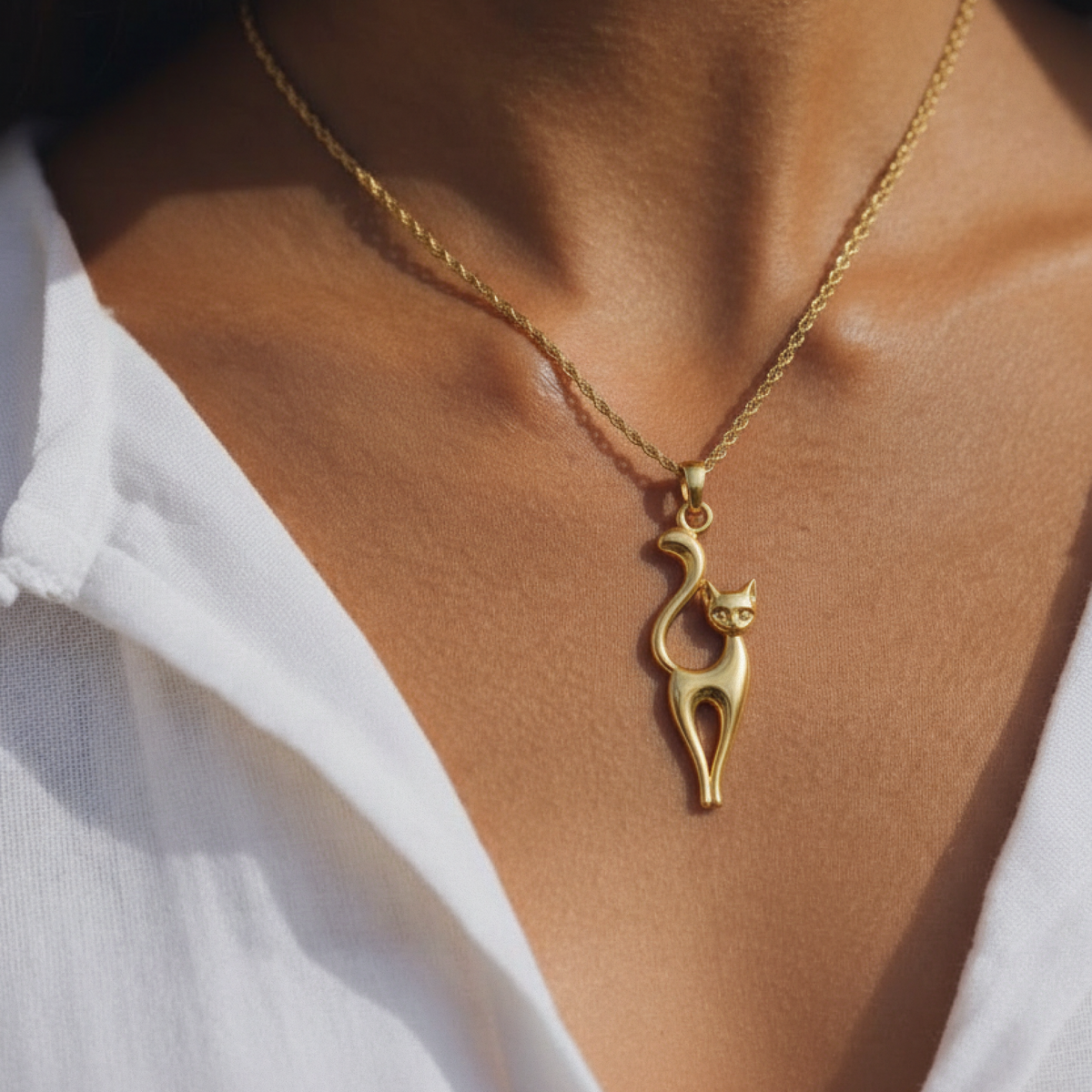 Mila Necklace in yellow gold, a cat silhouette pendant, worn at the collarbone with an open white linen shirt.
variant: yellow-gold