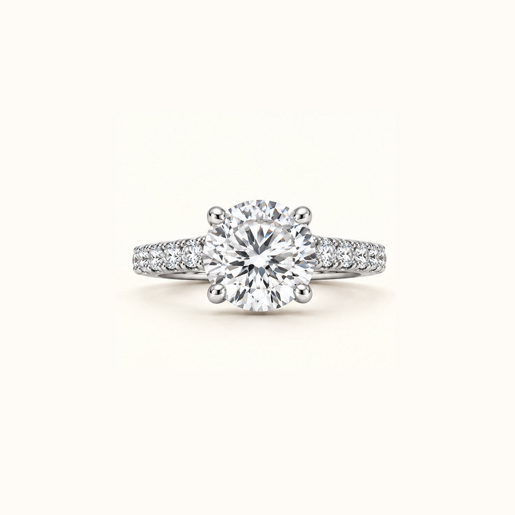 Noelle engagement ring in white gold with a round diamond in four claw prongs and a pavé diamond band, on a cream background
variant: white-gold
