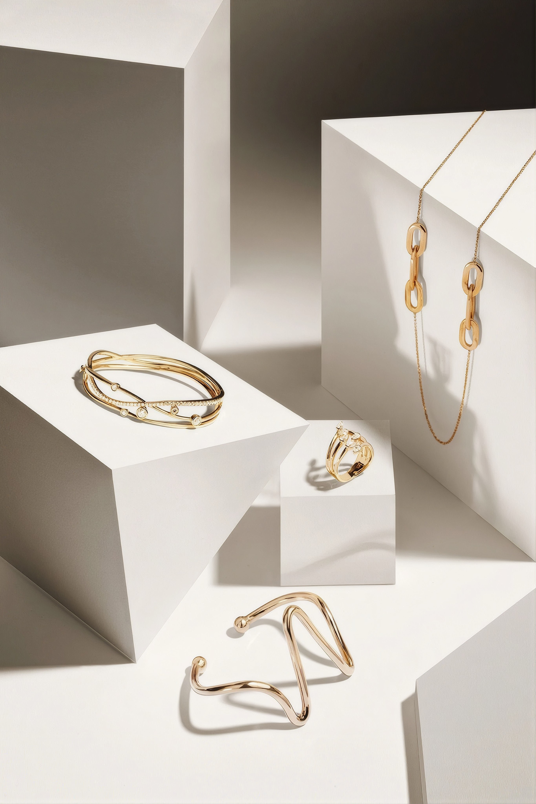 Gold jewelry including rings and bracelets on a geometric white and gray background